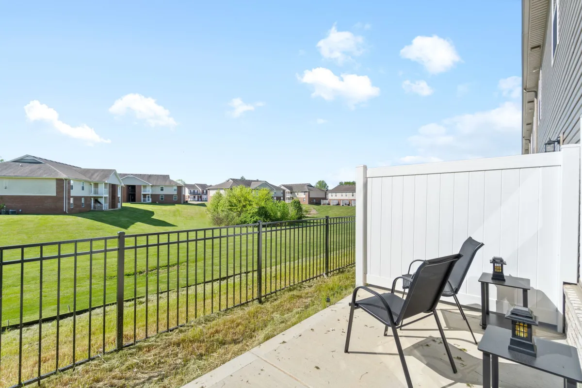 A cozy patio area with chairs and a small table, overlooking a lush green fenced yard. The scene suggests peaceful mornings with coffee or relaxed evenings with family, offering a private outdoor retreat.