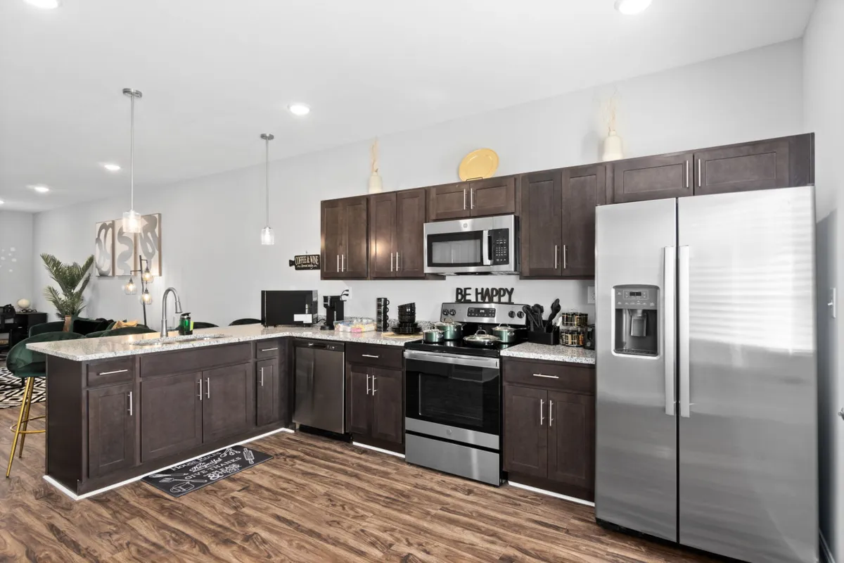An open-concept kitchen with a central island, sleek stainless steel appliances, and decorative elements like green plants and signage. The kitchen flows seamlessly into the adjacent living and dining space, emphasizing the home’s sociable layout.
