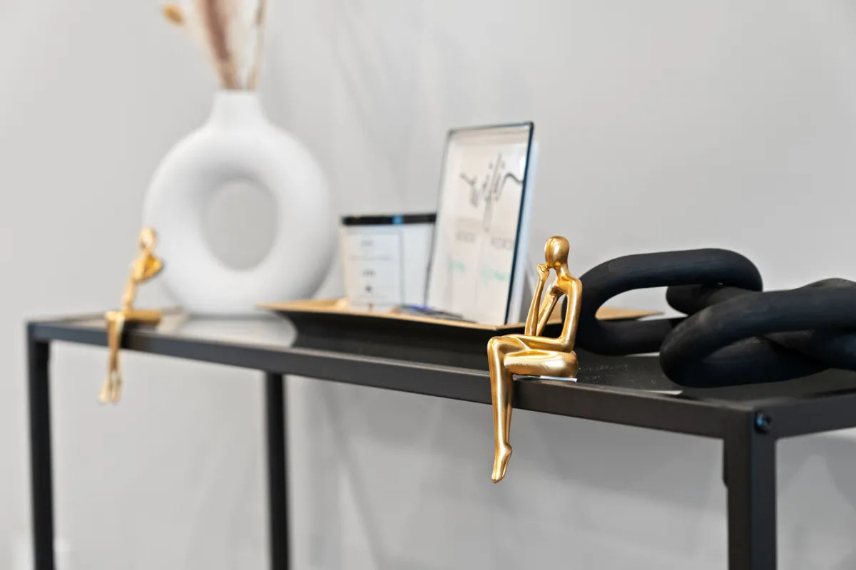 A stylish and sophisticated interior vignette featuring golden figurines, a black chain, a white vase, and framed artwork, set in an entryway or foyer area.