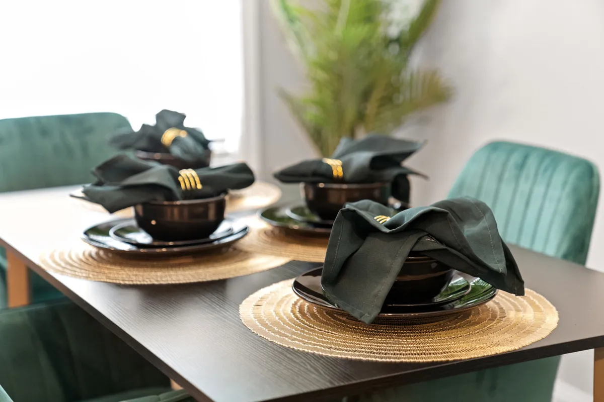 A warmly lit table elegantly set for dinner, surrounded by greenery, evoking an inviting atmosphere perfect for intimate meals and conversations. The focus on dinnerware and the ambiance suggests special evenings shared together.