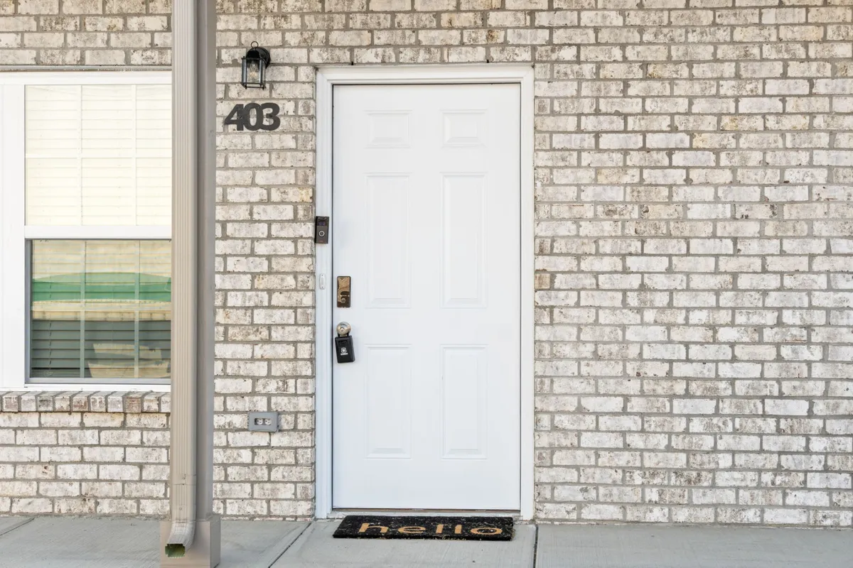 A close-up view of a white door set in a brick wall, complemented by a door mat. The simple, welcoming entryway hints at a secure and easily accessible entrance for guests.