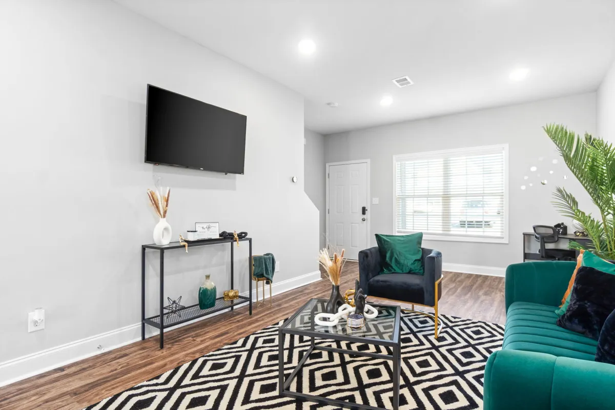 A modern, open-concept space featuring a green sofa, geometric rug, decorative plant, and a wall-mounted TV. This area is arranged for both relaxation and socializing, with a layout that supports easy flow between living and dining spaces. The decor is stylish yet inviting.