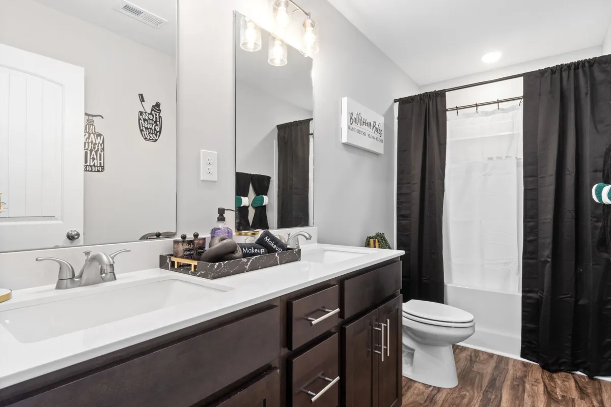 A spacious bathroom featuring a vanity with double sinks, a large mirror, and a black shower curtain. The layout feels both functional and luxurious, suggesting plenty of space and convenience for guests to refresh and revitalize.