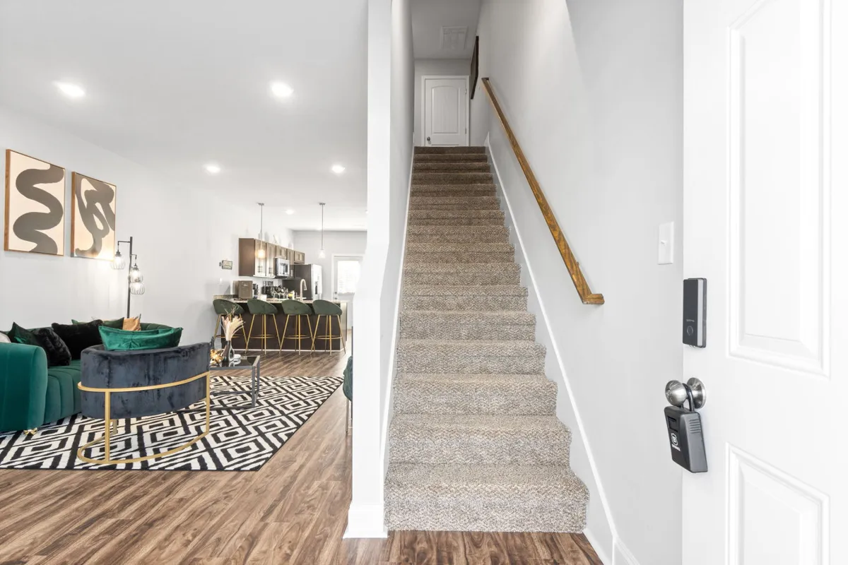 A stylish living area with a green velvet sofa, geometric rug, and modern staircase, inviting guests to entertain or relax. The setup is both contemporary and cozy, perfect for gatherings or quiet evenings.
