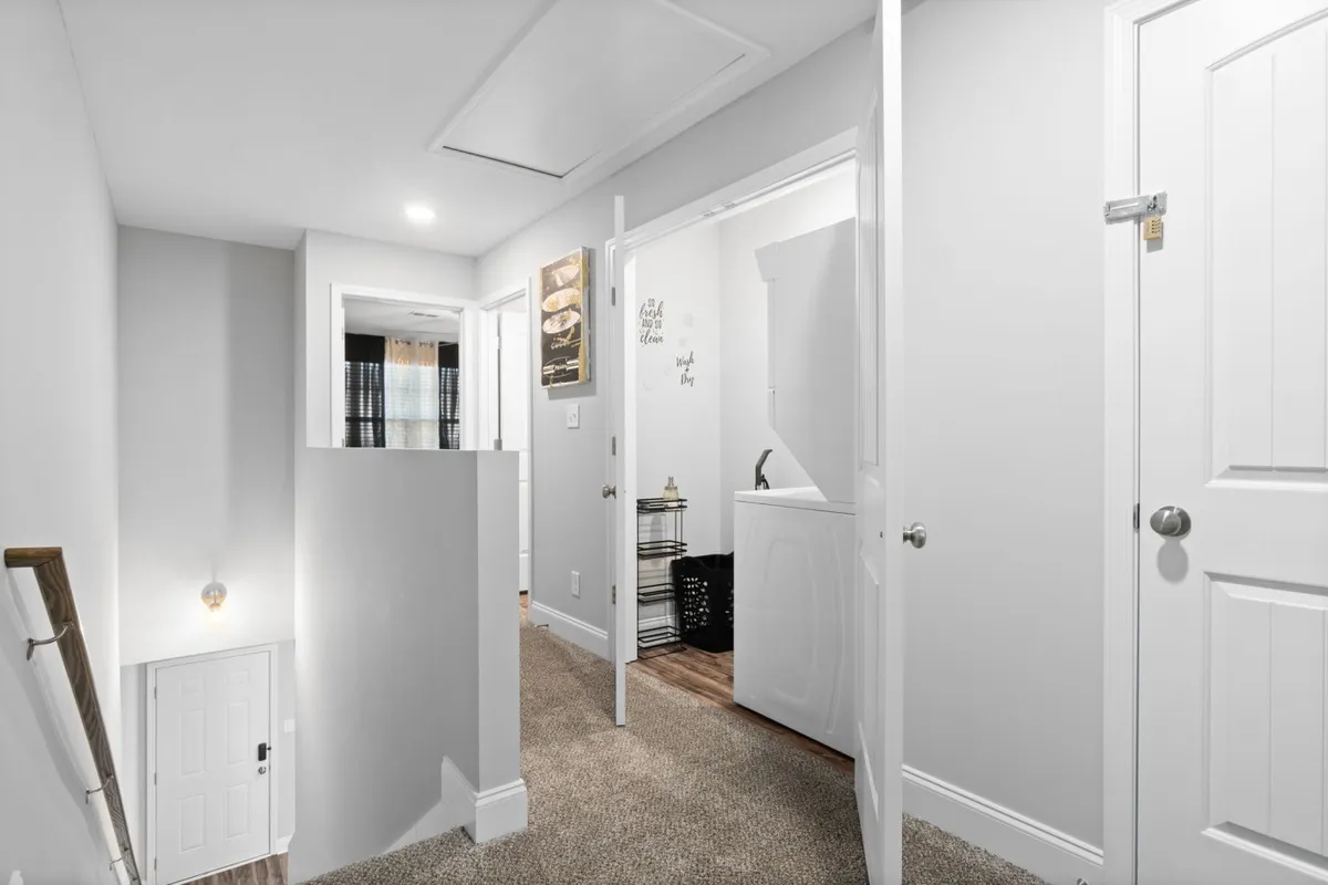 A practical and welcoming household scene featuring a laundry area, adjacent staircase, and open doorway. The setup conveys the essence of home life—organization, daily routines, and a sense of movement throughout the space.