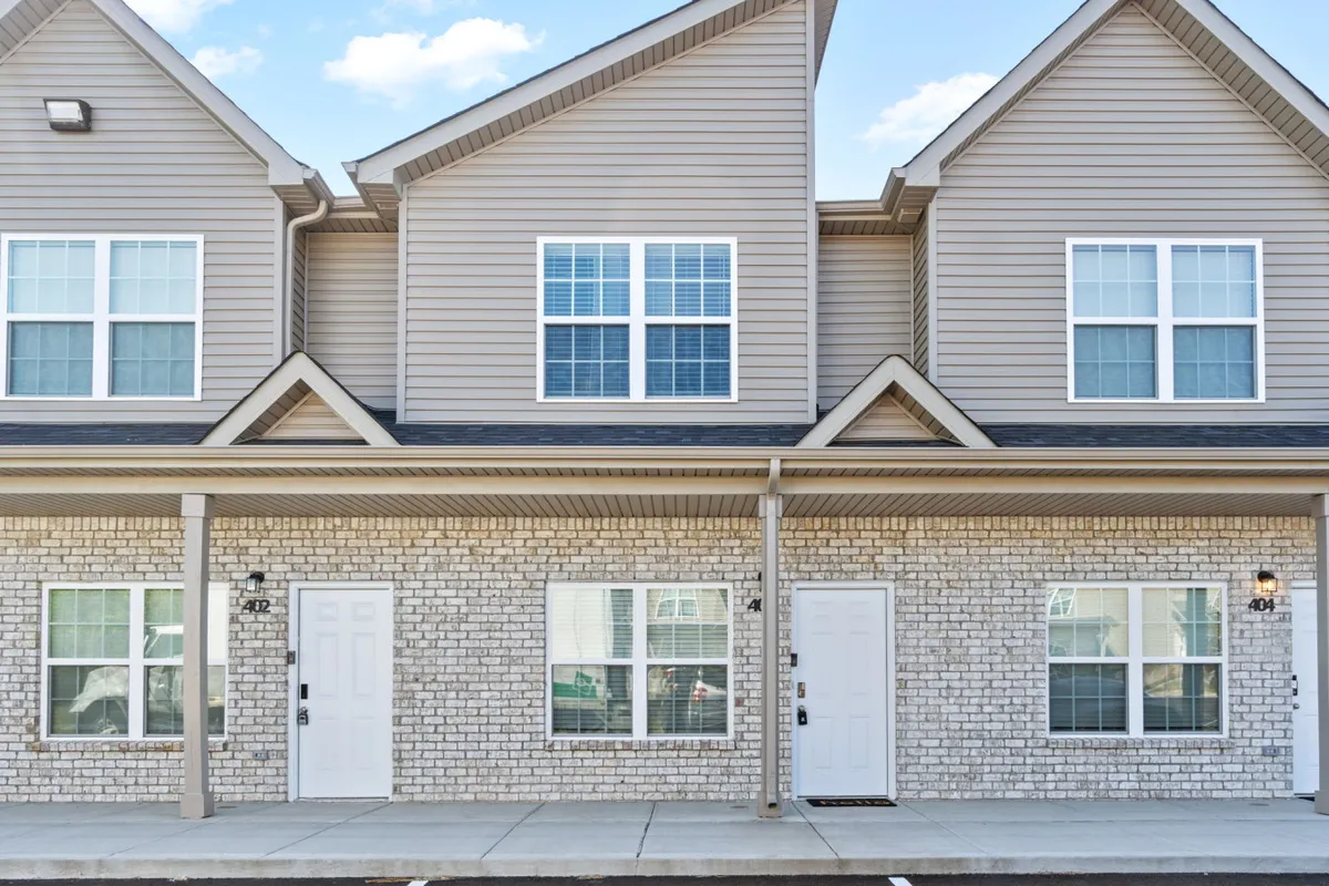 A view of the brick facade of the building with front doors and windows visible. The image signals a friendly arrival environment and hints at ample space for parking nearby.