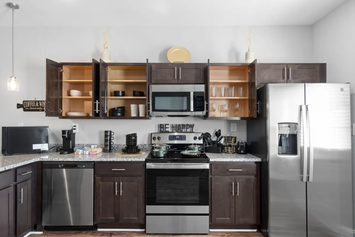 A cheerful, sunlit kitchen featuring stainless steel appliances, spacious granite countertops, open cabinets displaying neatly arranged dishware, and decorative touches that add warmth and character. The area looks perfect for both everyday meal prep and special gatherings.