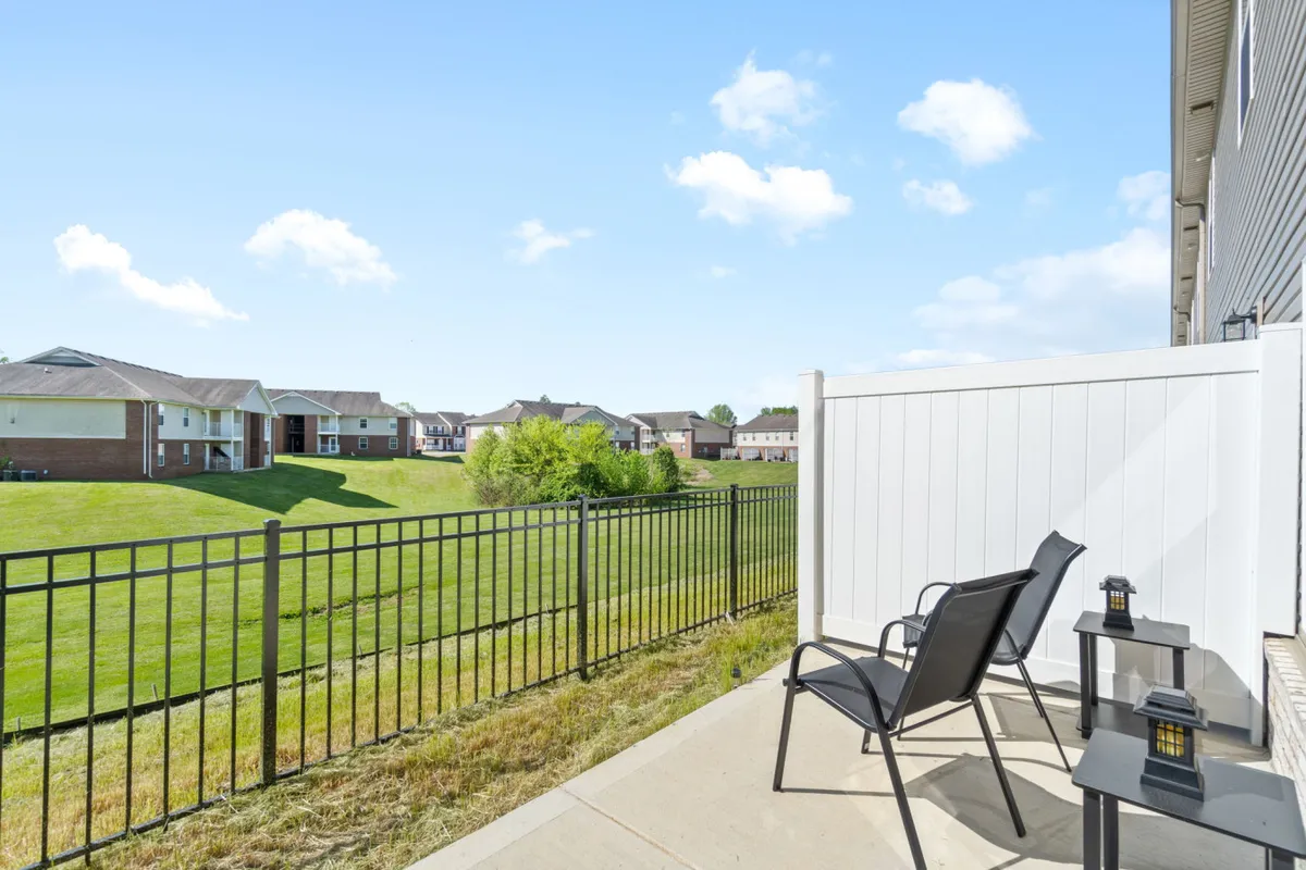 An inviting exterior scene featuring two black chairs and a small table set on a lush green lawn, all within a private fenced area. The tranquil setting is perfect for enjoying quiet moments outdoors, surrounded by nature.
